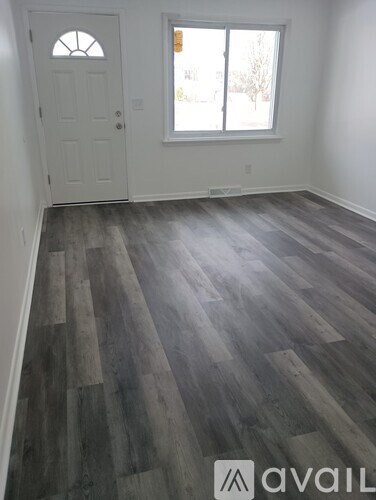 A room with a white door and a window with a view of trees outside.