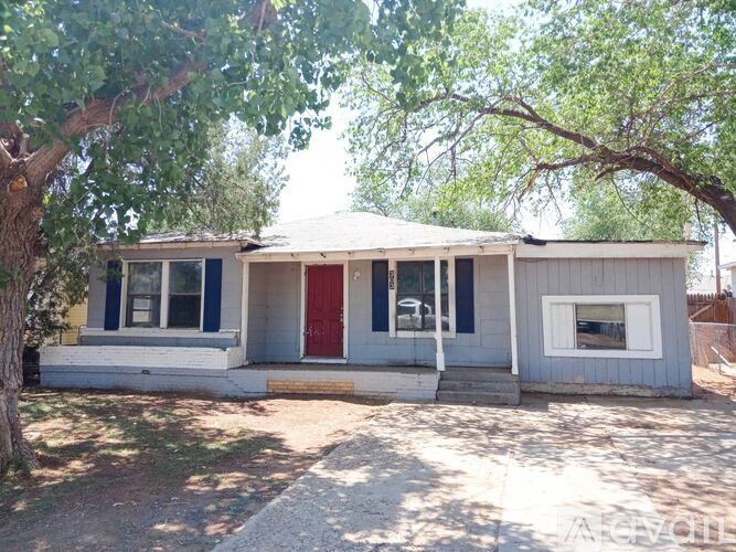 A small house with a red door is surrounded by trees.