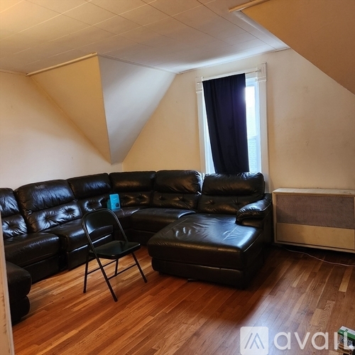 A black leather couch and chair in a room with wooden floors and a window with curtains.