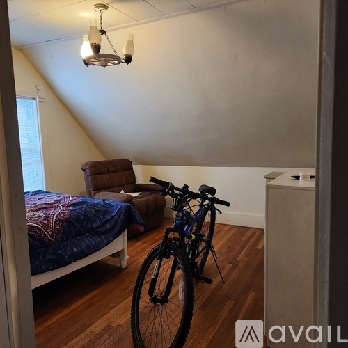 A bicycle is leaning against a wall in a room with a bed and a chair.