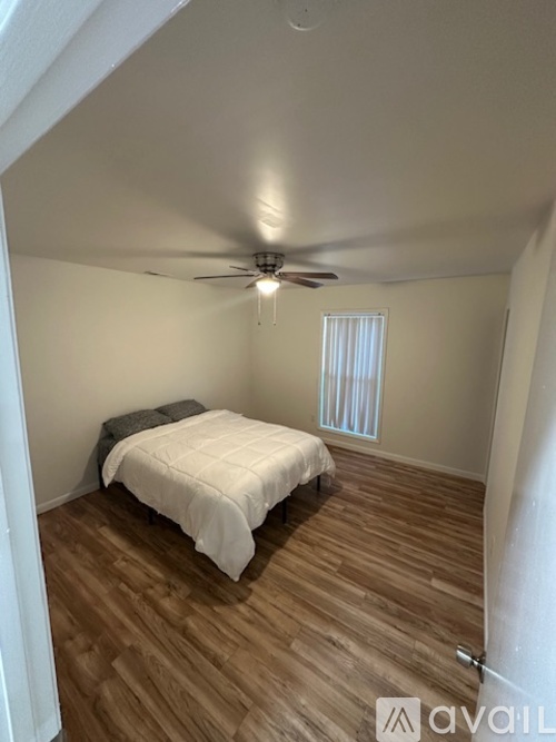 A bedroom with a bed, wooden floor, and a ceiling fan.