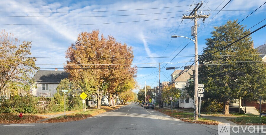 A street with a yellow sign and trees with autumn leaves.