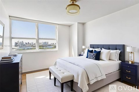A bedroom with a large bed and a window overlooking a city skyline.
