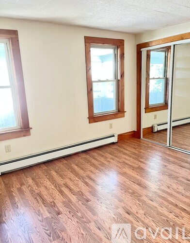 A room with wood flooring and two windows.