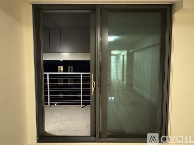 A glass door with a handle is open, revealing a hallway with a metal gate and a building in the background.