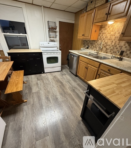 A kitchen with a white stove top oven, black dishwasher, and wooden cabinets.