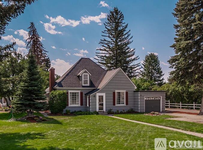 A house with a grey roof and a white fence is surrounded by greenery.
