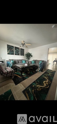 A living room with a black and gold rug and a ceiling fan.