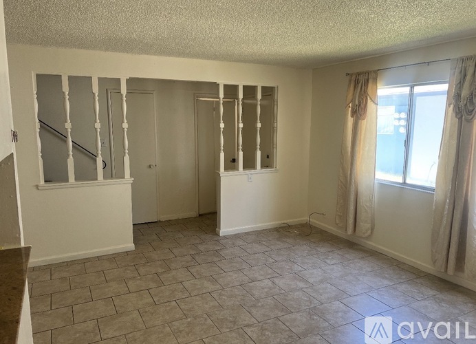A spacious room with a staircase and a window with curtains.