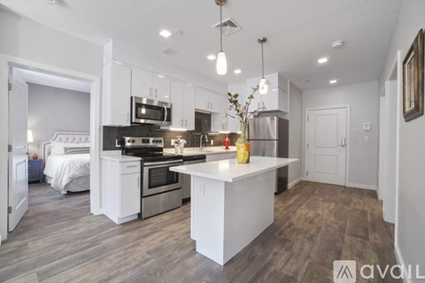 A modern kitchen with a large island and a bedroom in the background.