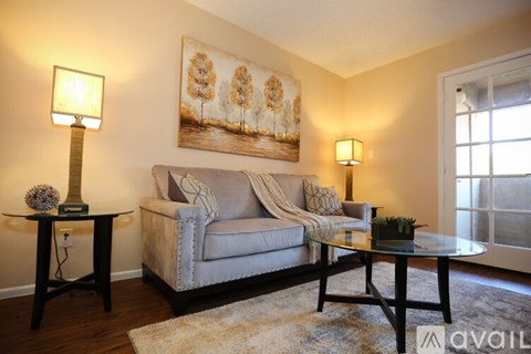 A living room with a grey couch, a painting of a tree, and two lamps.