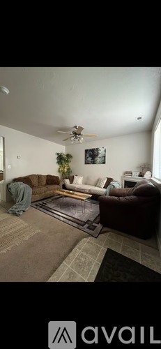 A living room with a brown rug and a ceiling fan.