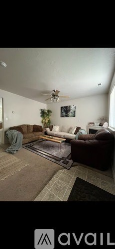 A living room with a brown rug and a ceiling fan.