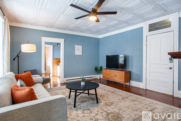 A living room with a grey couch, a black coffee table, a wooden cabinet, a flat screen TV, and a ceiling fan.