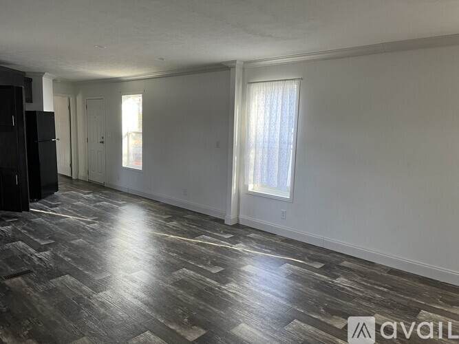 A room with wooden flooring and a window with white curtains.