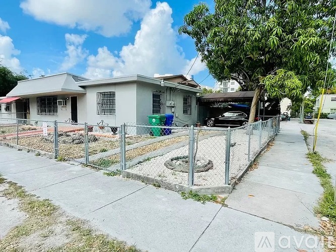 A house with a fenced yard and a tree in front.