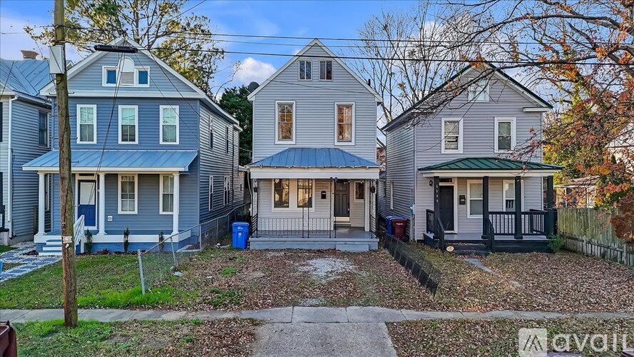 A blue house with a white door and windows is in front of a tree.