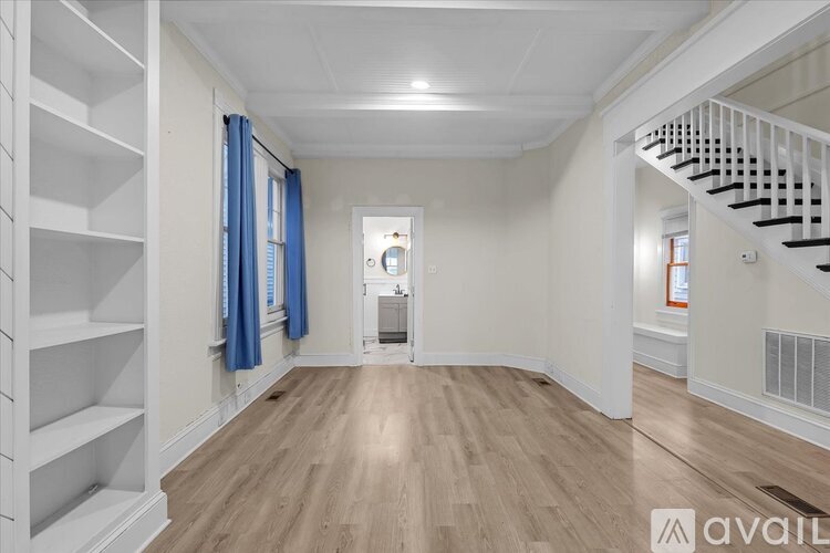 A spacious room with a staircase on the right and a doorway leading to another room.