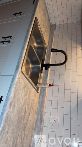 A stainless steel sink in a white tiled bathroom.