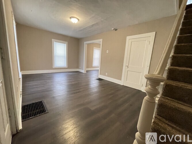 A spacious room with wooden floors and a staircase leading to another room.