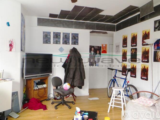 A room with a TV, a chair, a desk, a bicycle, and posters on the wall.
