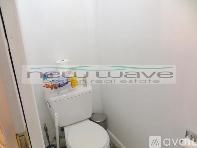A white toilet in a small bathroom with a sign that says "nuwave real estate".