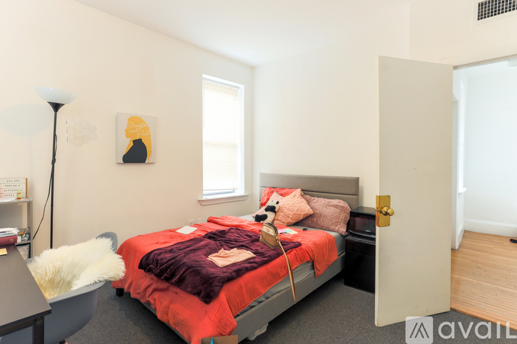 A bedroom with a red bedspread and a white chair.