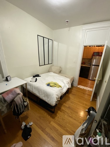 A bedroom with a bed, desk, and a doorway leading to a kitchen.