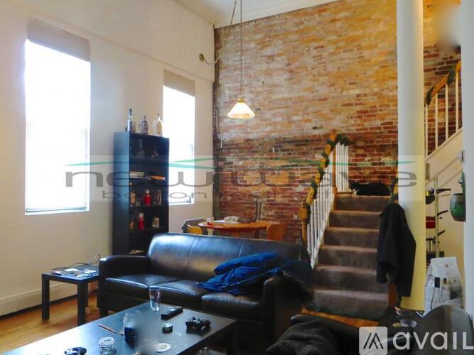 A living room with a black leather couch and a wooden staircase.