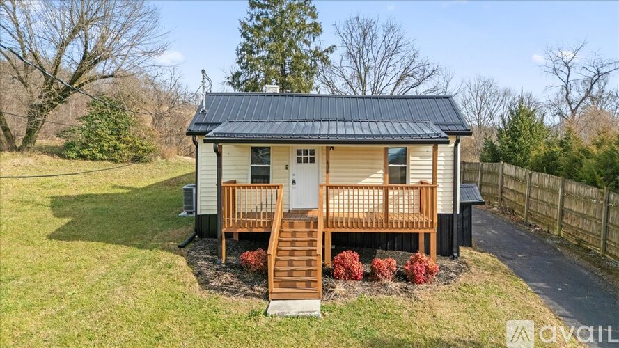 A small house with a porch and a black roof is surrounded by a grassy area and trees.