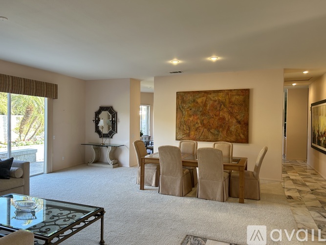 A living room with a glass coffee table and a large painting on the wall.