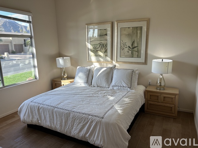 A bedroom with a large bed, two lamps, and two framed pictures on the wall.