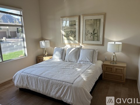 A bedroom with a large bed, two lamps, and two framed pictures on the wall.