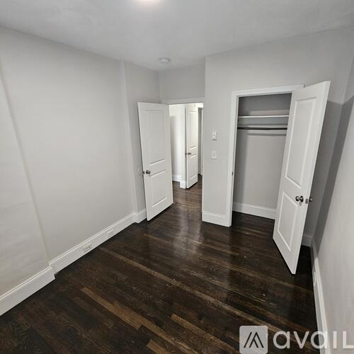 A room with white walls and wooden floors with two open doors.