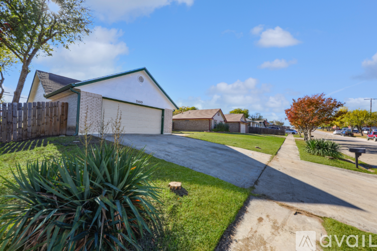 A house with a white garage door is surrounded by a fence and a grassy area with a tree.