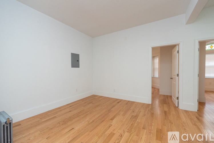 A room with wooden floors and white walls, with a doorway leading to another room.