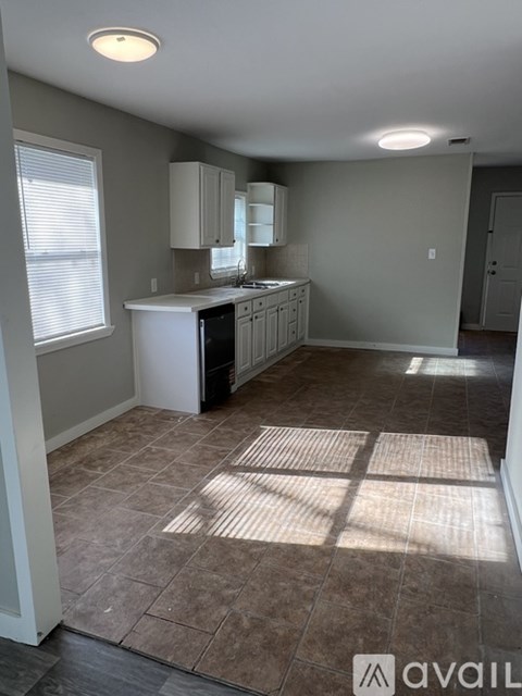 A room with a grey floor and walls, leading to another room with a brown floor.