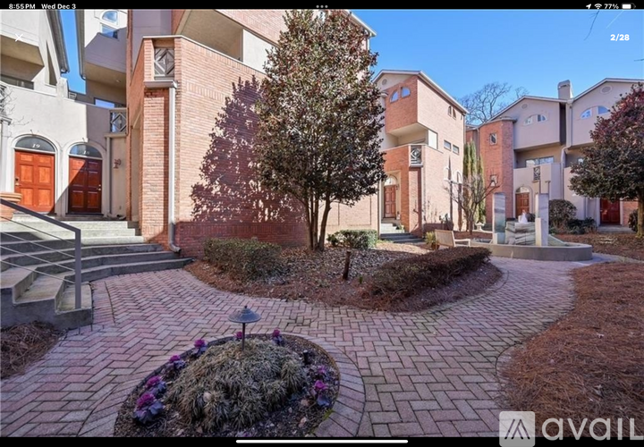 A brick walkway leads to a building with a tree in the middle of a flower bed.
