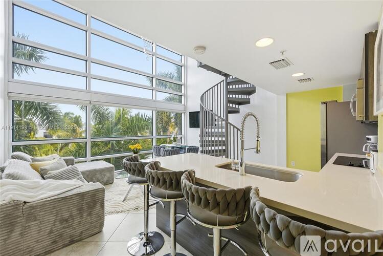 A modern kitchen with a spiral staircase and a large window overlooking a palm tree-filled landscape.
