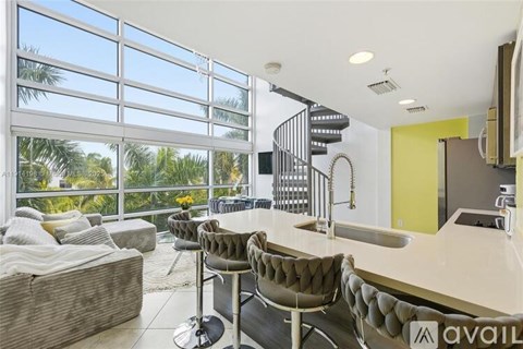 A modern kitchen with a spiral staircase and a large window overlooking a palm tree-filled landscape.