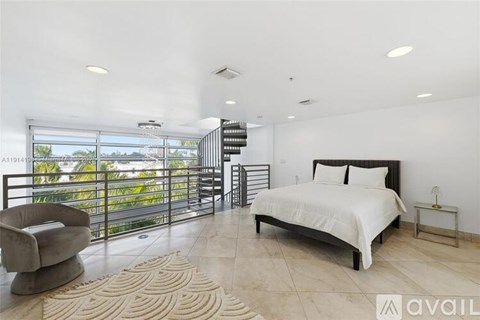 A bedroom with a large bed and a balcony with a view of trees.
