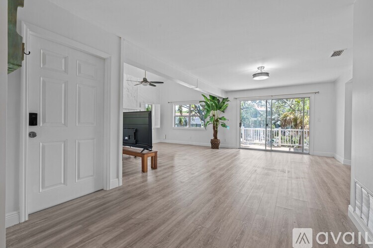 A spacious living room with a television and a sliding glass door leading to a balcony.