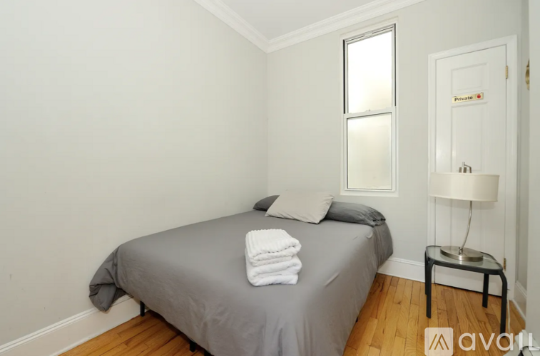 A bedroom with a bed, a nightstand with a lamp, and a window.