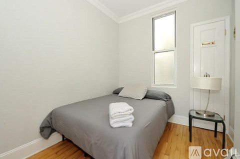 A bedroom with a bed, a nightstand with a lamp, and a window.