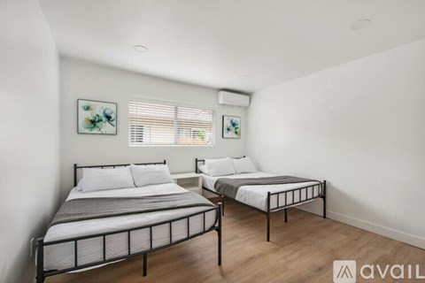 A bedroom with two beds and a window with blinds.