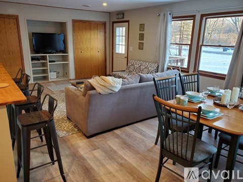 A living room with a grey couch, a wooden cabinet, a television, and a dining table with chairs.