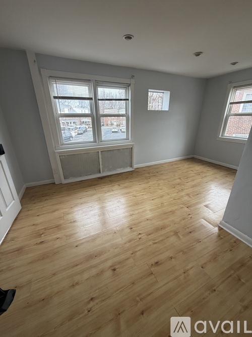 A room with wooden flooring and two windows.