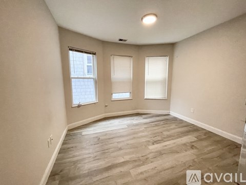 A spacious room with wooden flooring and three windows.