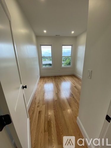 A hallway with wooden floors and white walls leading to a door with a window.