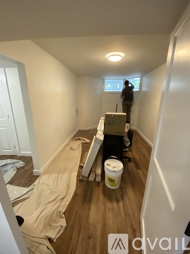 A man is painting a wall in a room with a bucket of paint on the floor.